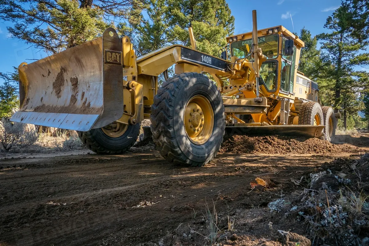 Yellow motor grader blading a dirt road
